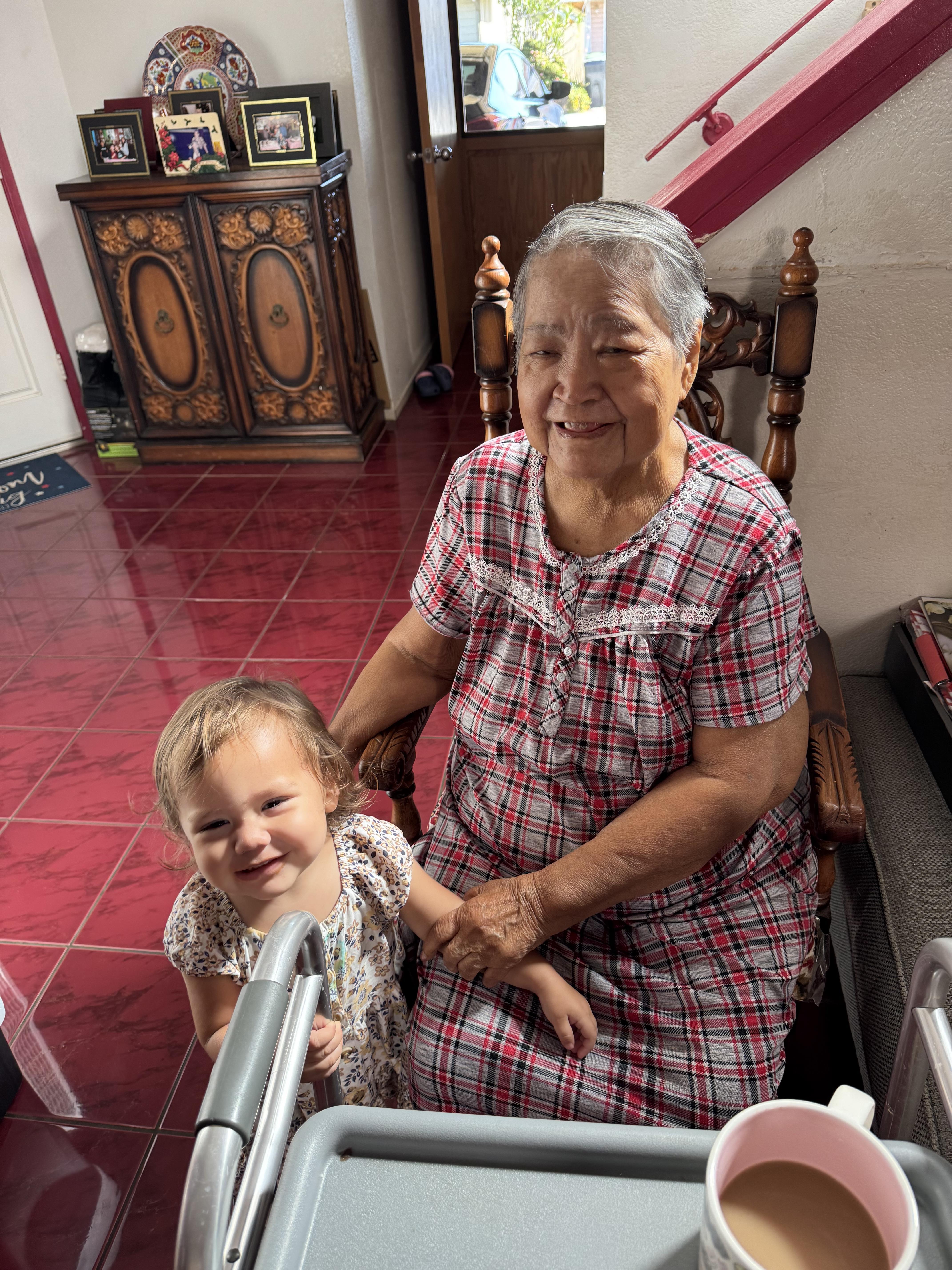 A grandmother enjoys playful time with her smiling grandchild in a warm interior.