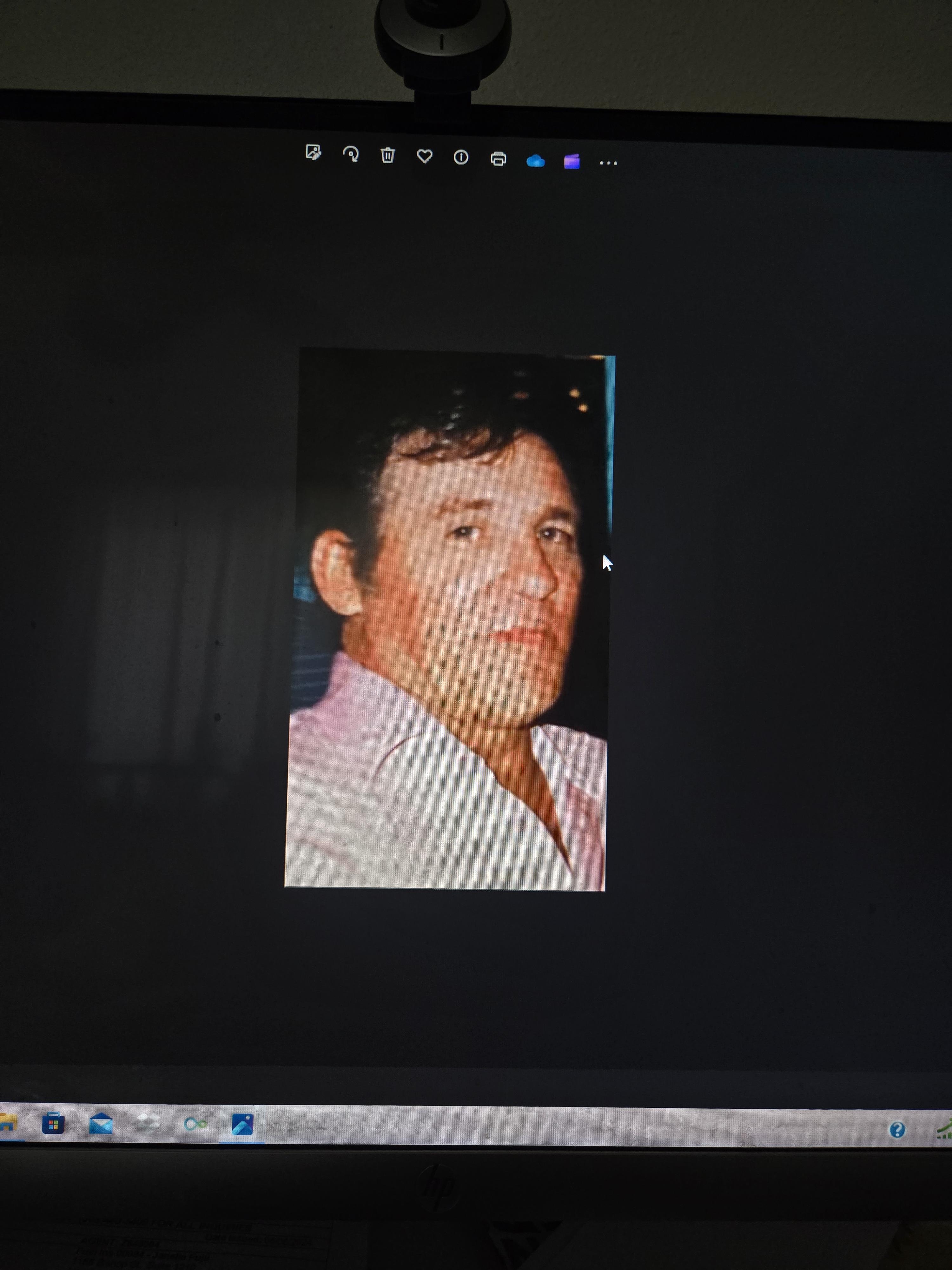 A man with dark hair smiles confidently, wearing a light-colored shirt. The background is dark.