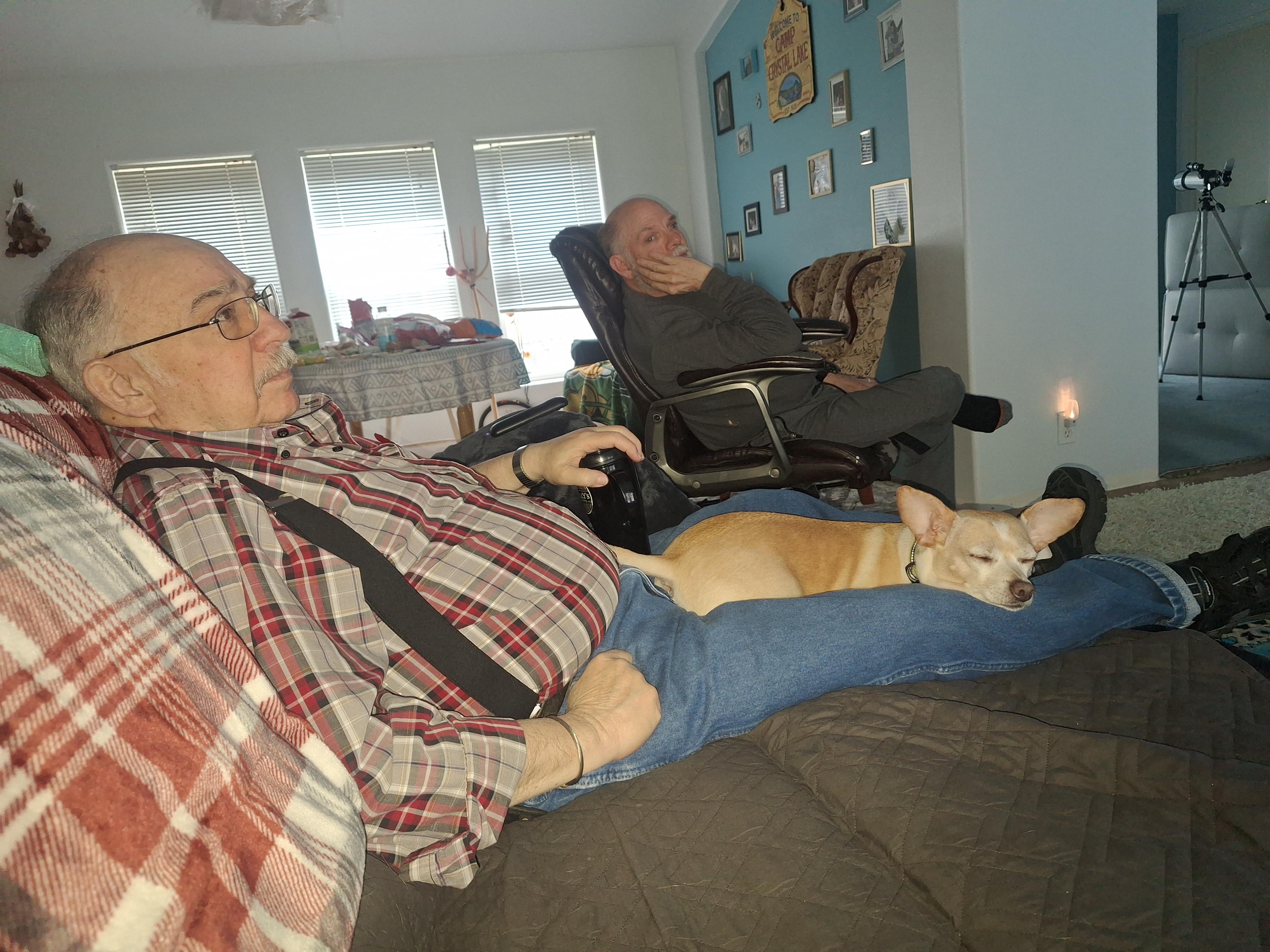 An elderly man enjoys a moment of relaxation at home with his small dog resting comfortably.