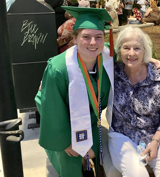 A man in a graduation cap and gown posing with an old woman
