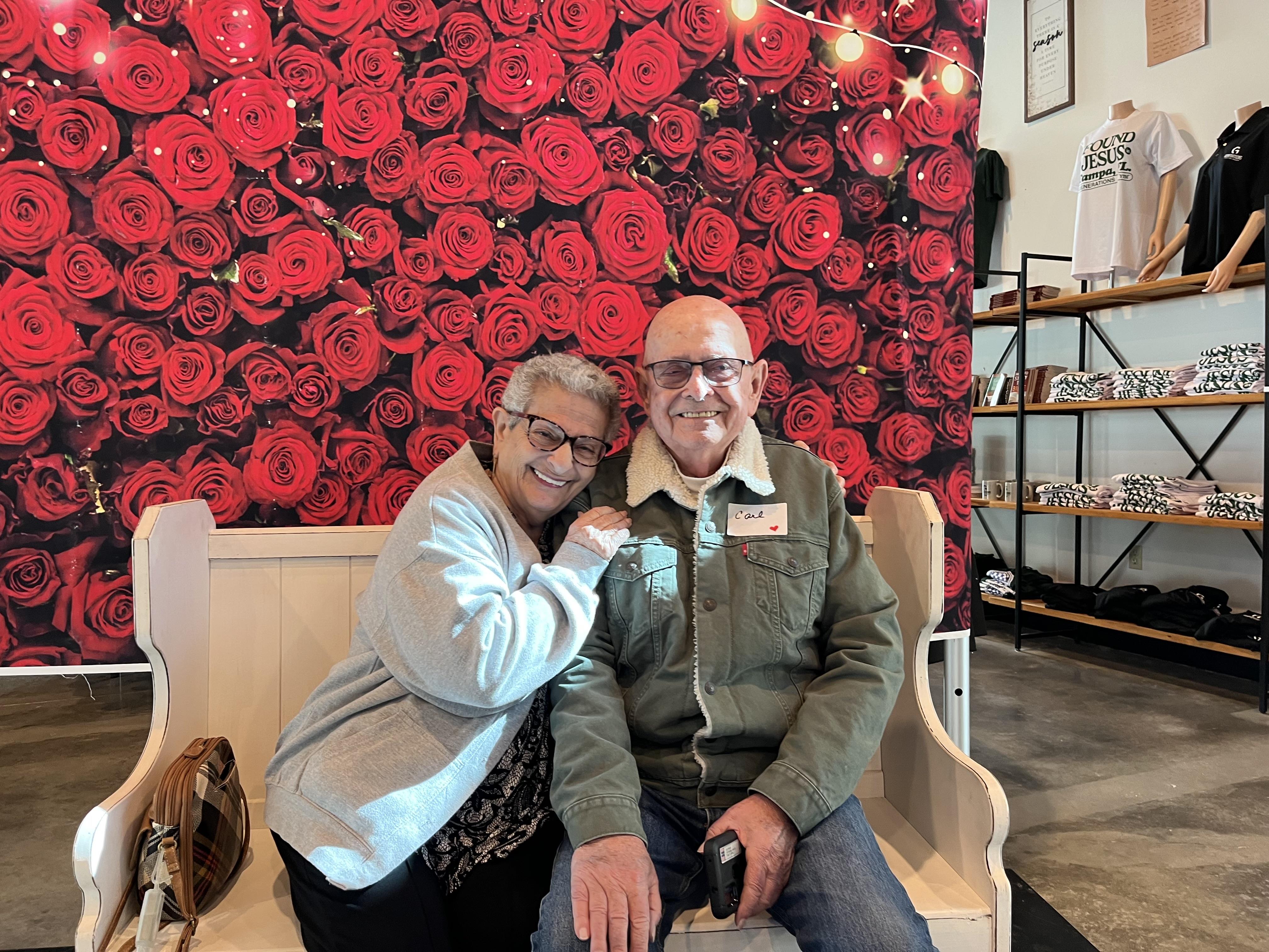 Happy couple enjoys their time together while posing near a colorful flower wall indoors.