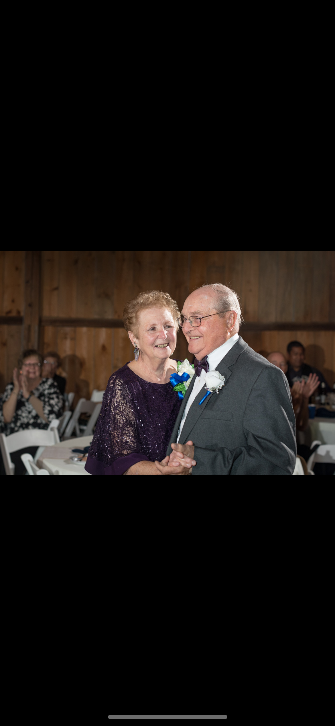 A couple dances lovingly amid friends and family in a cozy, warm setting.