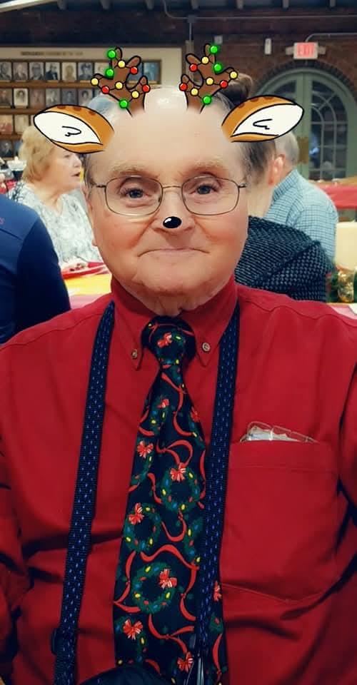 A man in a red shirt and festive tie enjoys a holiday celebration with friends nearby.