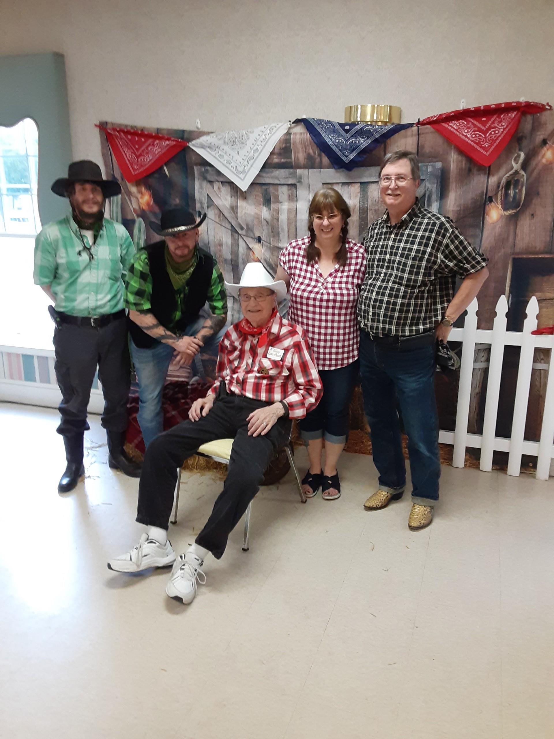 Friends in cowboy attire celebrate with smiles and decorations at a community event.