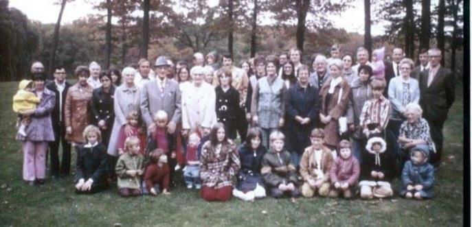 Family gathering in a park, surrounded by fall foliage and diverse outfits.