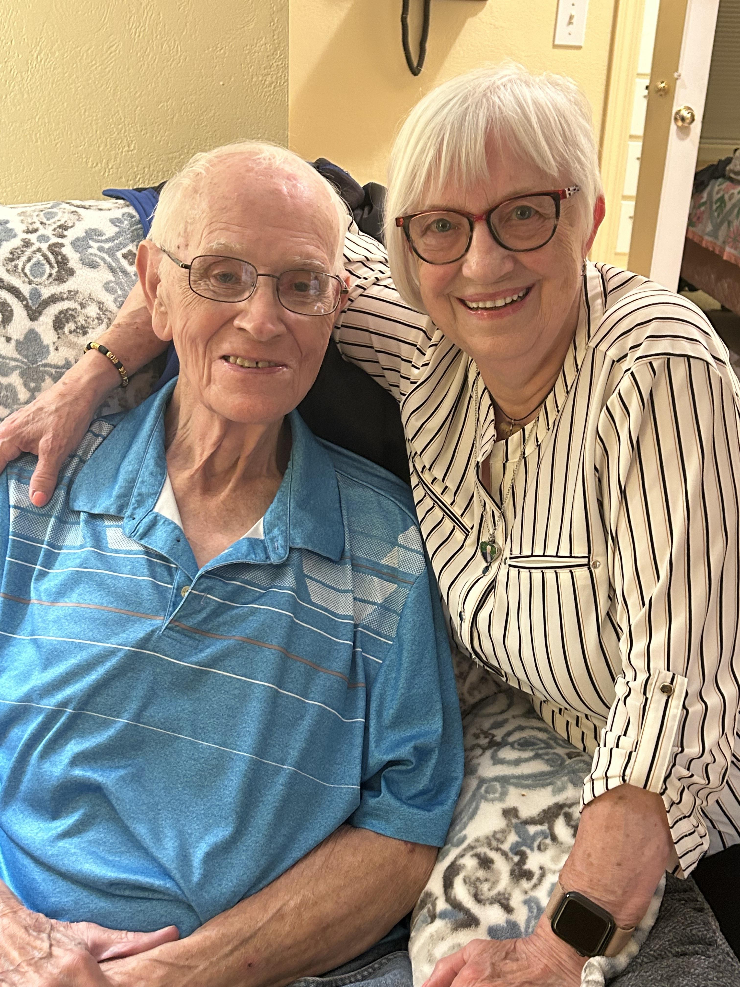 An elderly couple enjoys a cheerful moment while sitting on a couch in a cozy living area.
