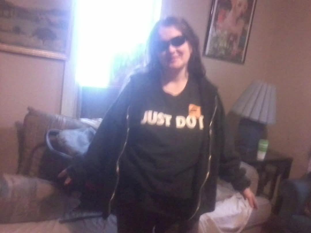 A woman stands confidently in a stylish outfit while wearing sunglasses indoors near a window.