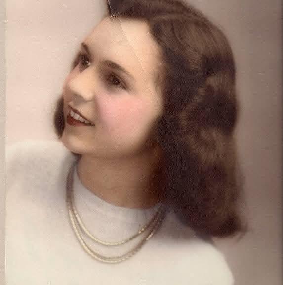A young woman poses gracefully with wavy hair, wearing a pearl necklace and smiling warmly.