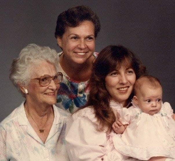 Four women of different generations smile warmly, celebrating family bonds with a baby in embrace.