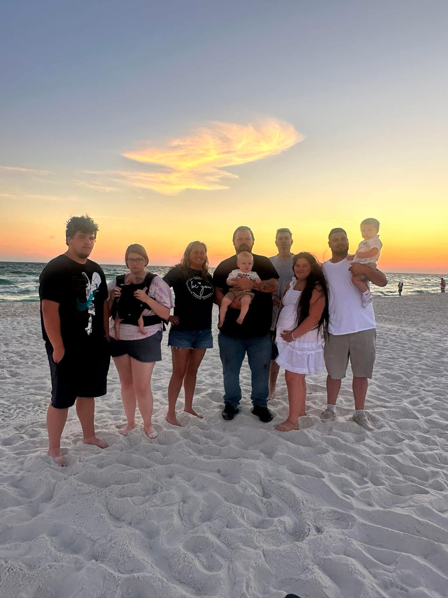Group of eight people enjoying time together at the beach with a beautiful sunset backdrop.