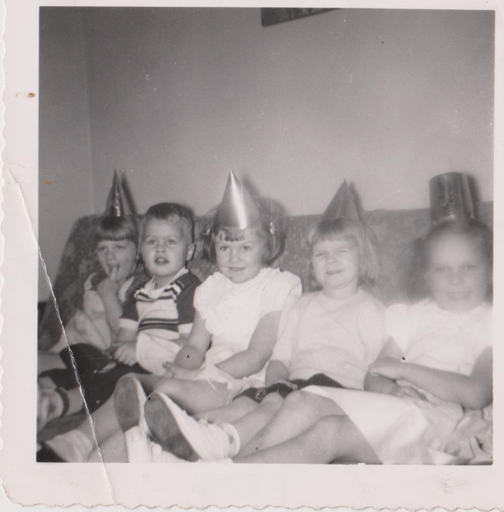 Five young children wear colorful hats while enjoying a birthday celebration at home.