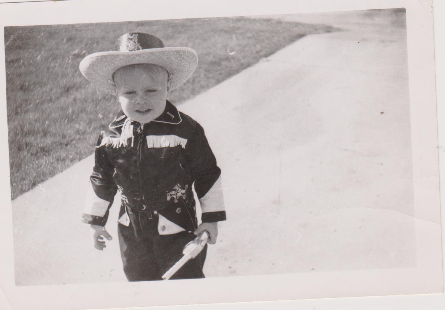 Child in cowboy attire walks happily on a sunny path, bringing joy to the surrounding area.