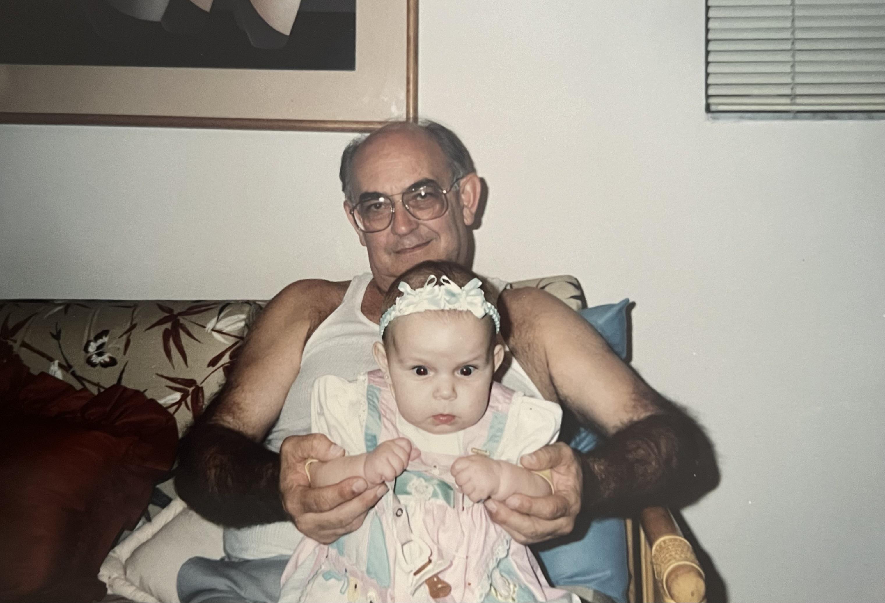 A grandfather smiles as he holds his baby granddaughter in a comfortable seating area.