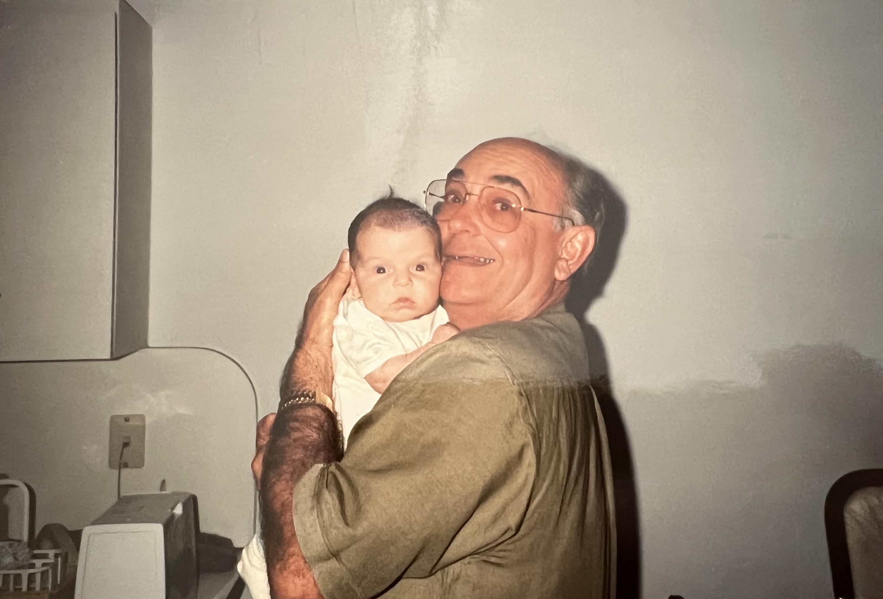 A joyful grandfather holds a newborn baby close, sharing a moment of love and connection indoors.