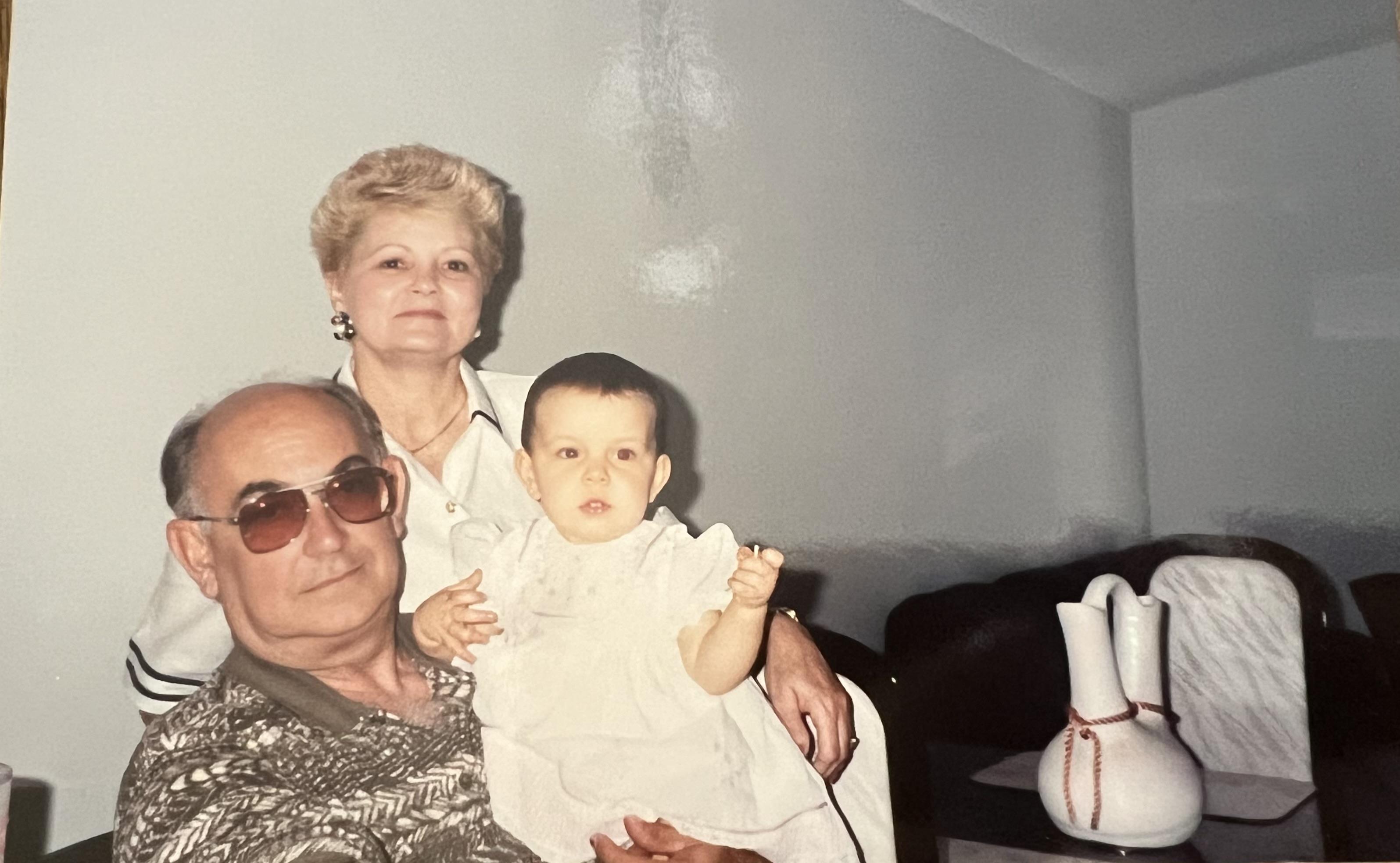 An elderly couple is holding a baby in a cozy living room filled with furniture.