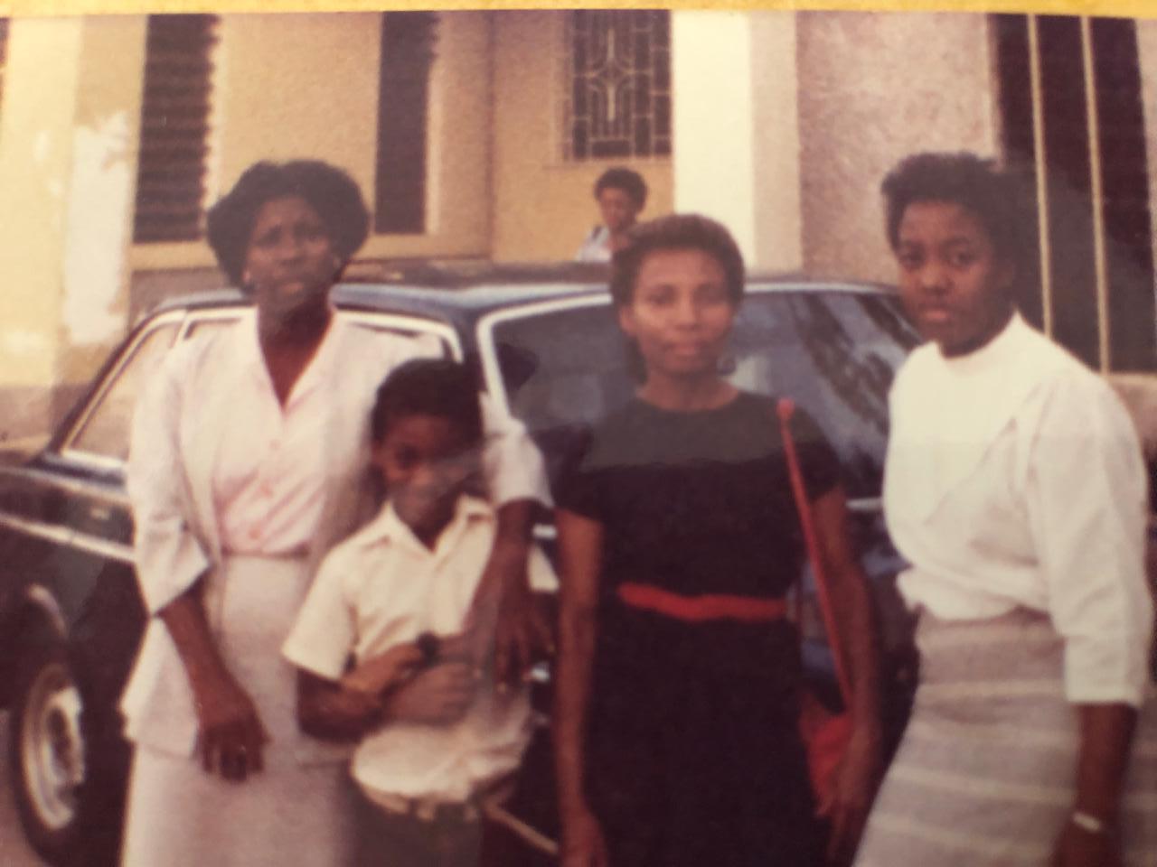 A cheerful family poses together with a classic car in a lively setting during daytime.