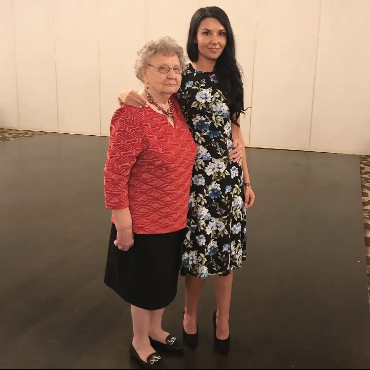 Two women smile for a photo together, one in a floral dress and the other in a red sweater.