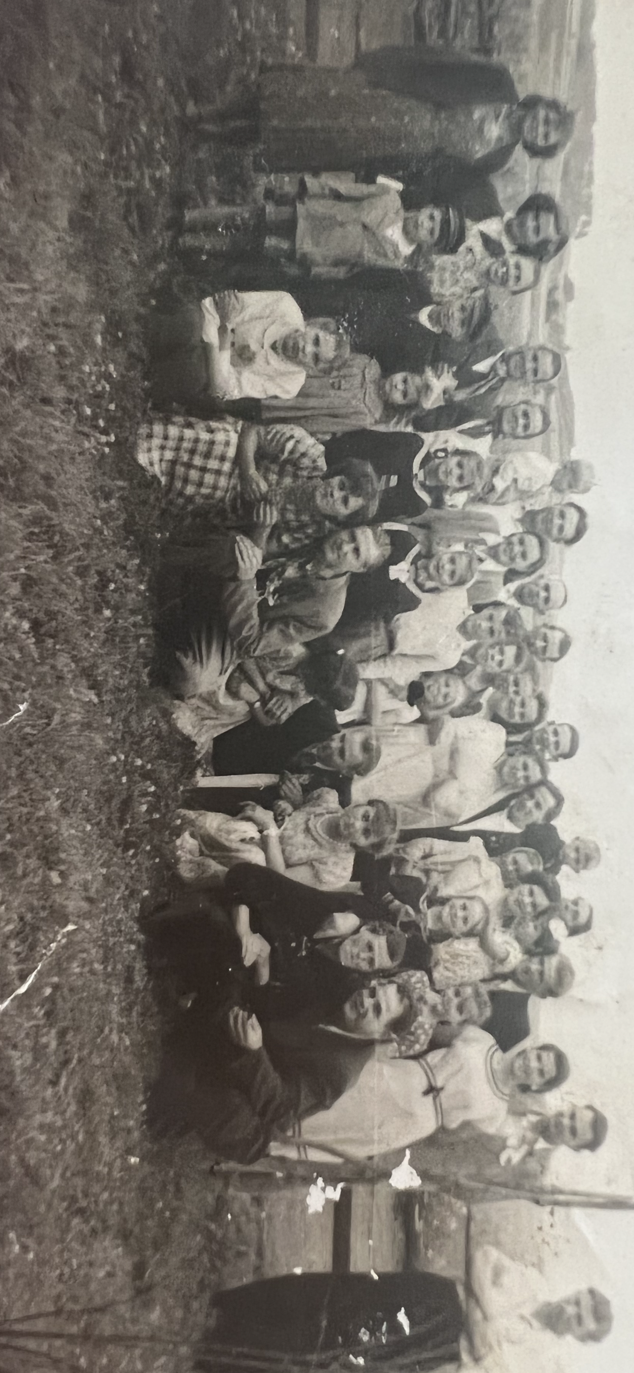A large gathering of women and children smiles in a rural area surrounded by greenery.