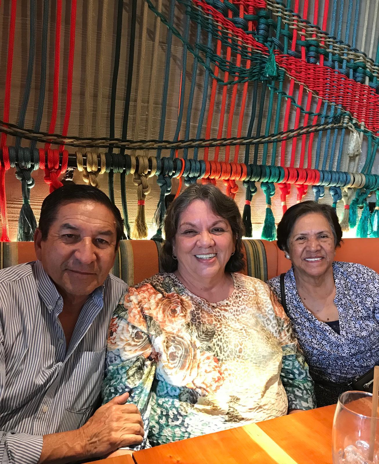 Three friends smile and celebrate together at a vibrant restaurant with decorative patterns.
