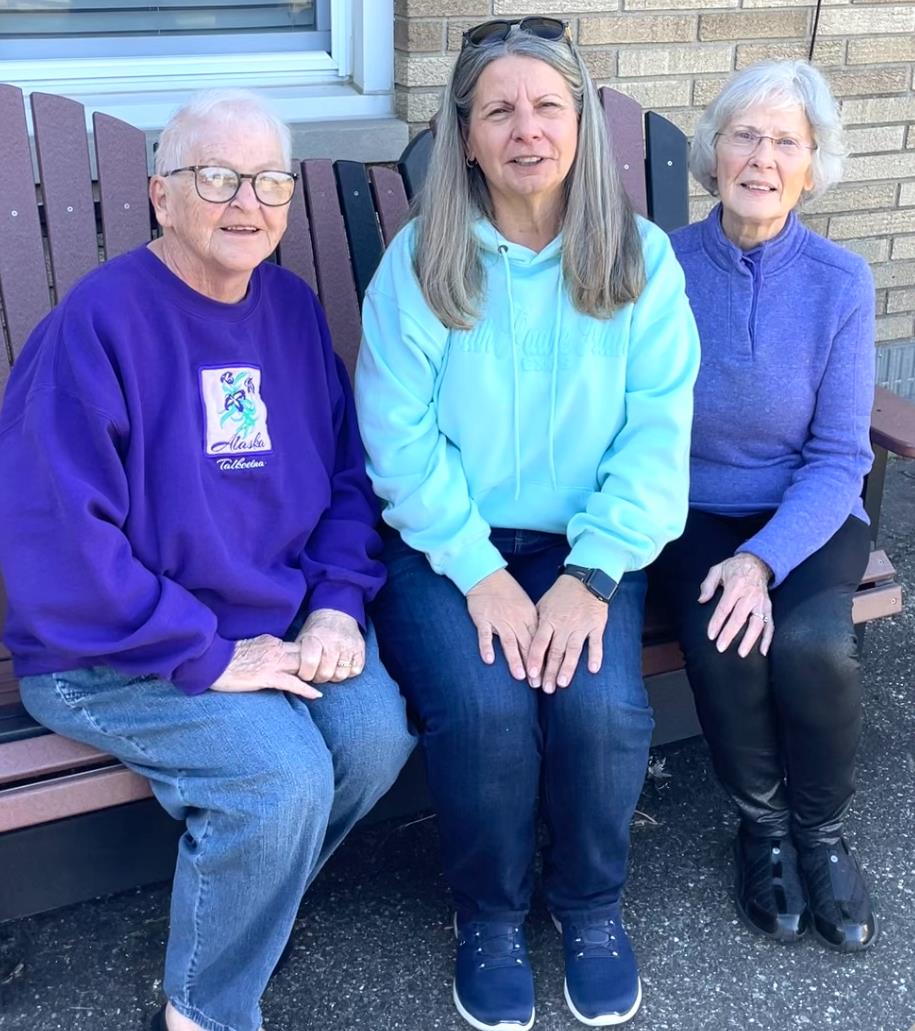 Three women sit on a bench, smiling happily while enjoying the warm weather outdoors.