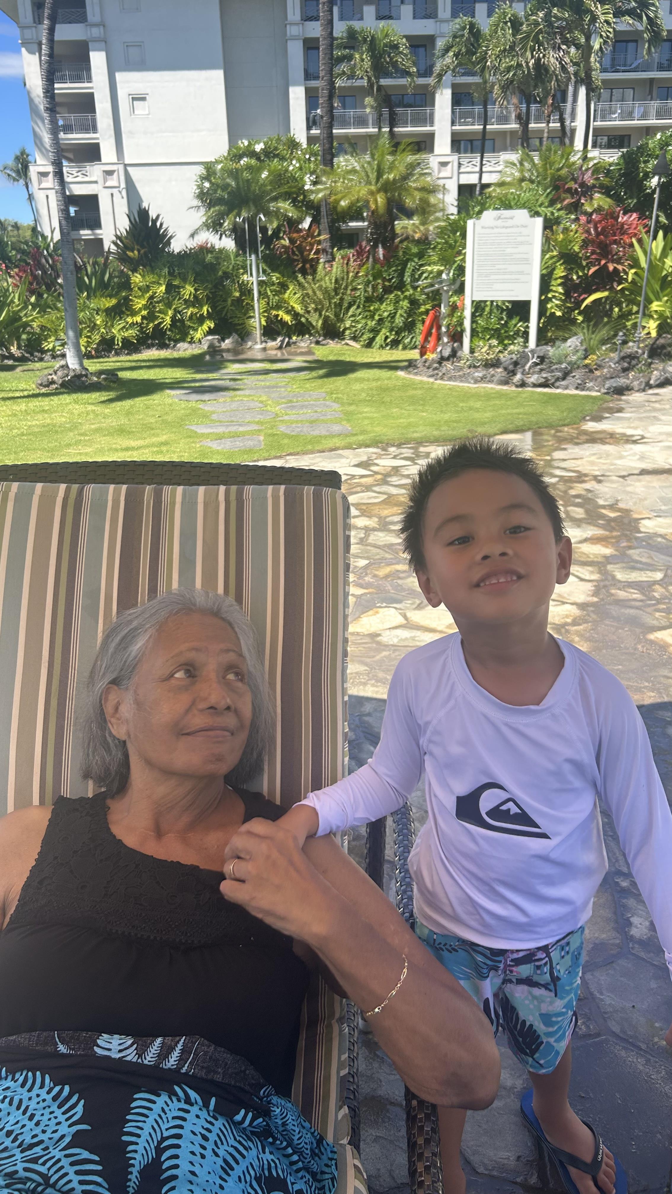 An elderly woman relaxes in the sun, while a young child enjoys the afternoon beside her.