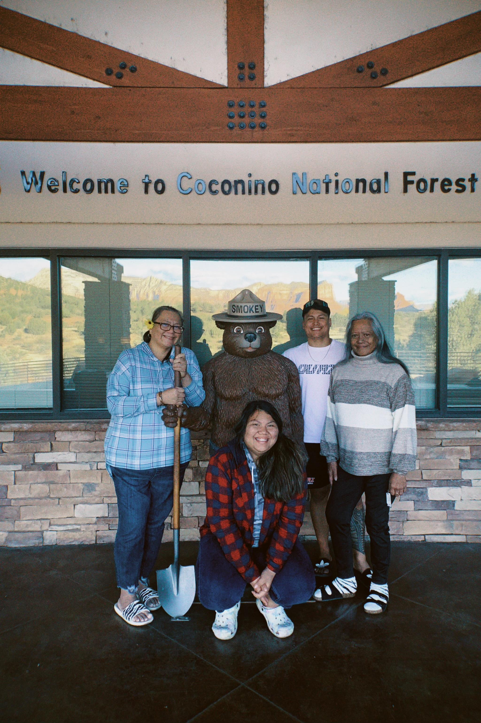 Group of friends pose happily with a ranger statue at Coconino National Forest welcome center.