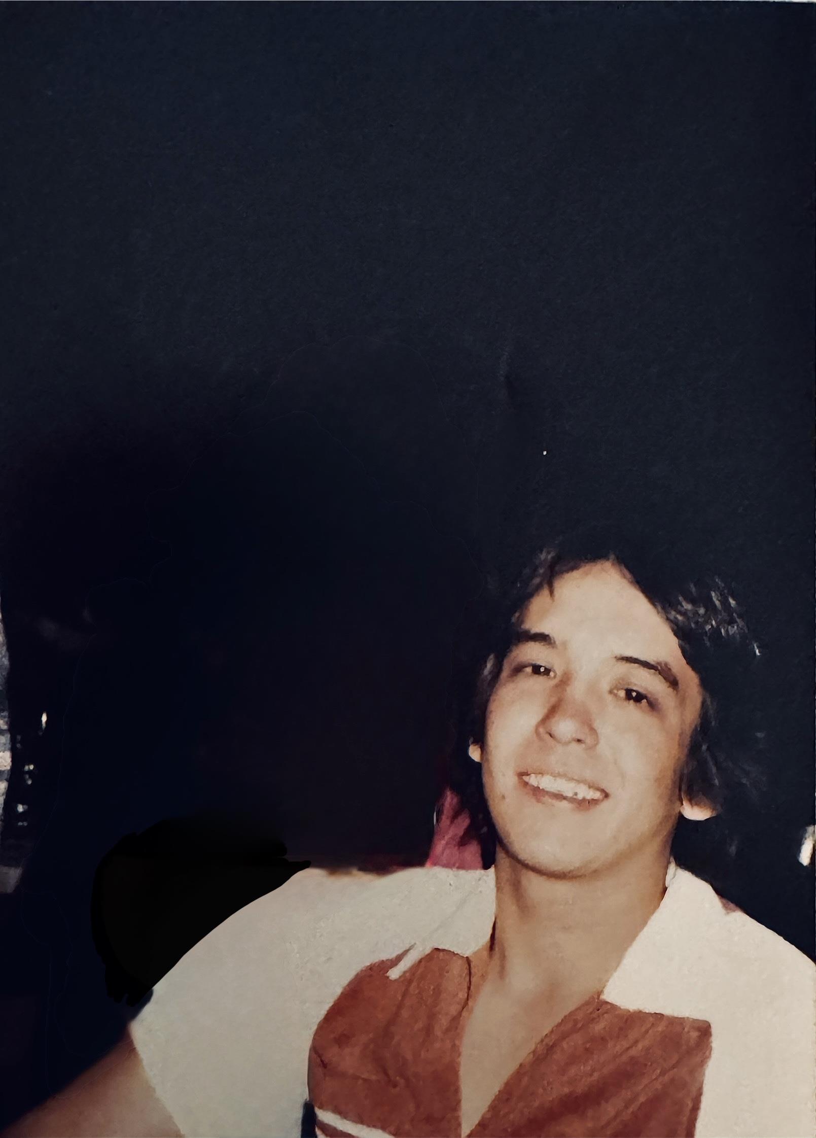 A young man with dark hair is joyfully smiling while seated at a social gathering.
