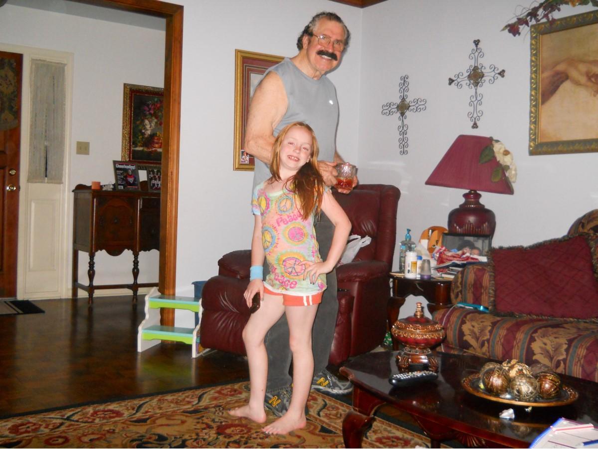 An adult stands playfully behind a child in a cozy living room decorated with furniture and art.