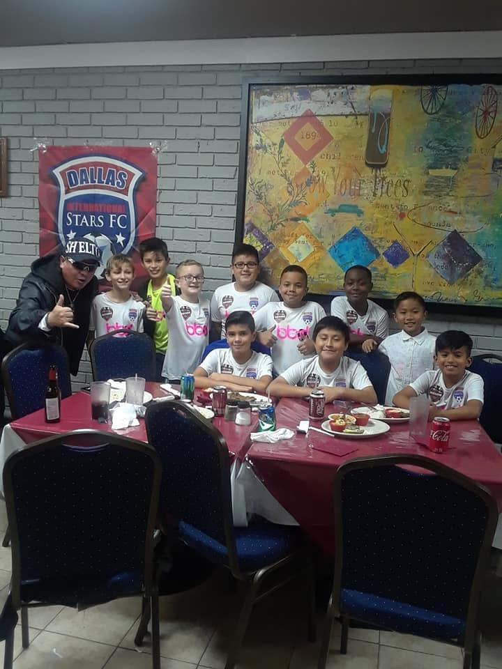 Children wearing soccer jerseys enjoy a festive meal with friends and coaches, celebrating teamwork.
