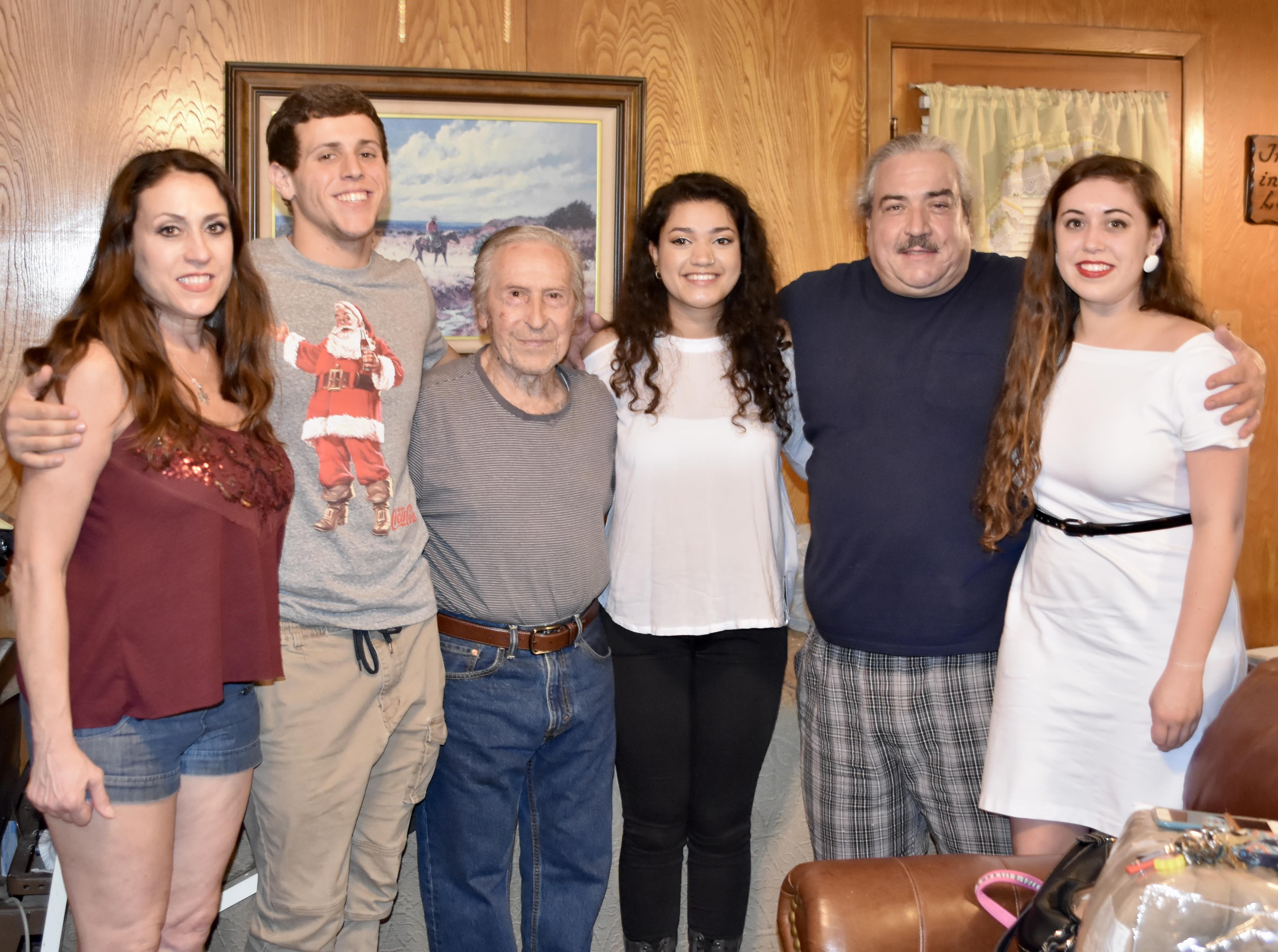 Six family members gather in a warm living room, sharing smiles and enjoying each other's company.