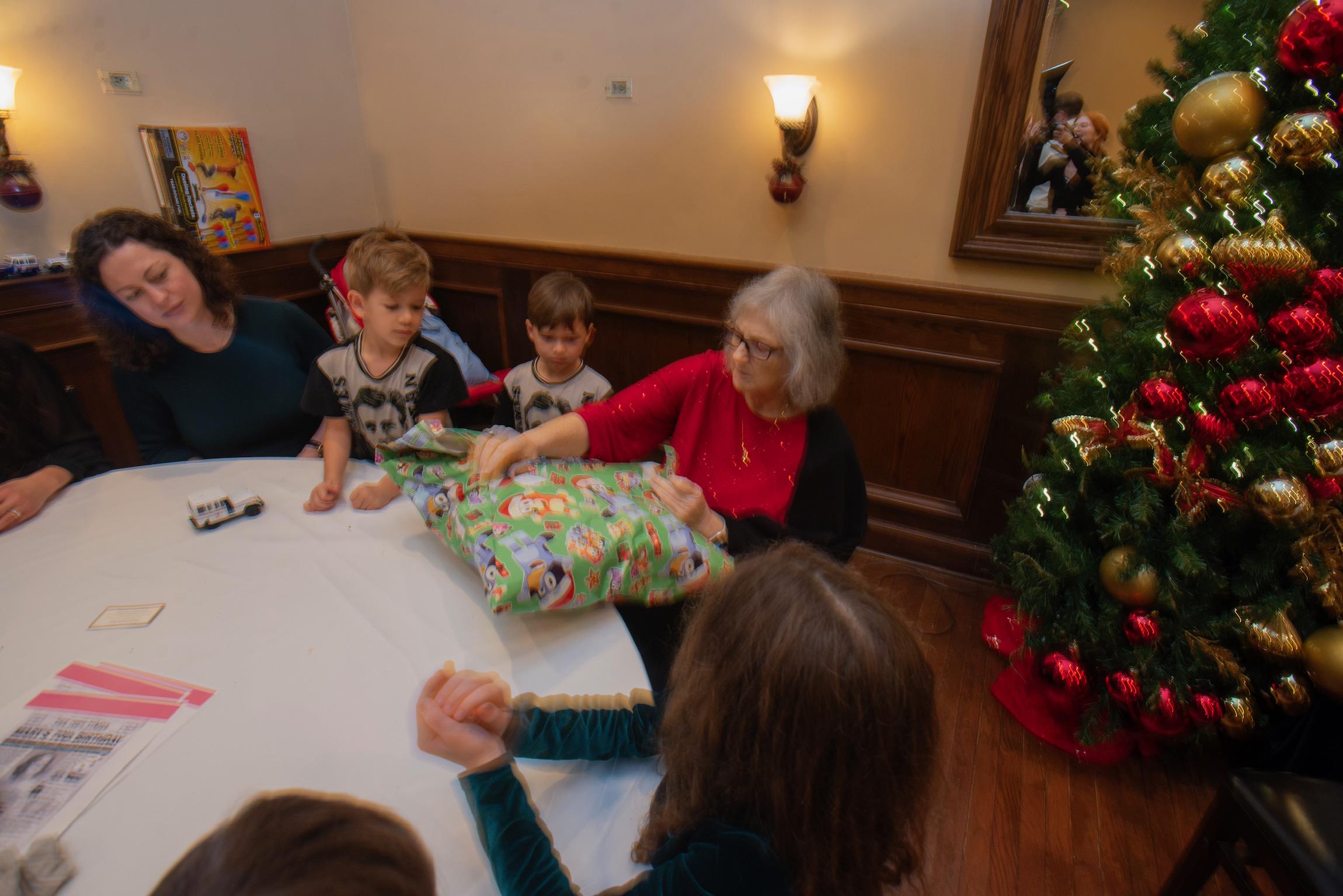 Family members enjoy unwrapping presents together at a decorated table during the holiday season.
