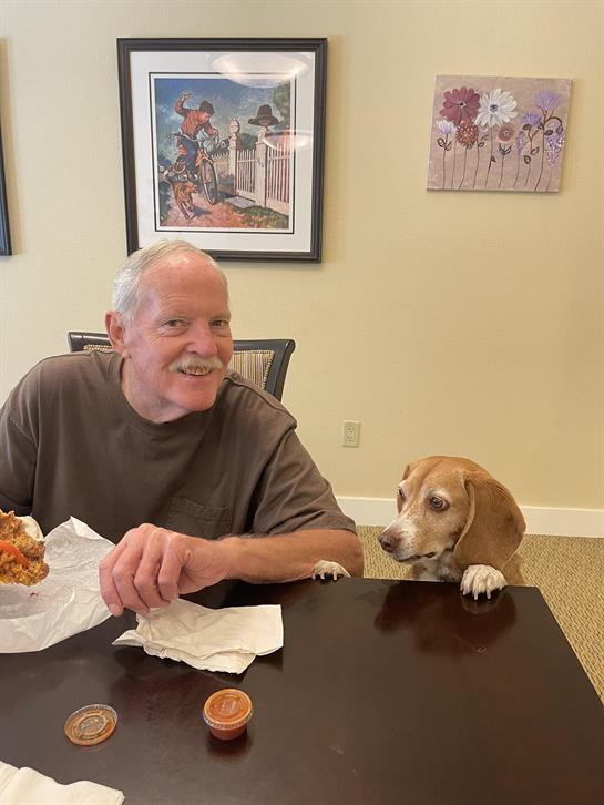 A dog sitting at a table with a man sitting at a table
