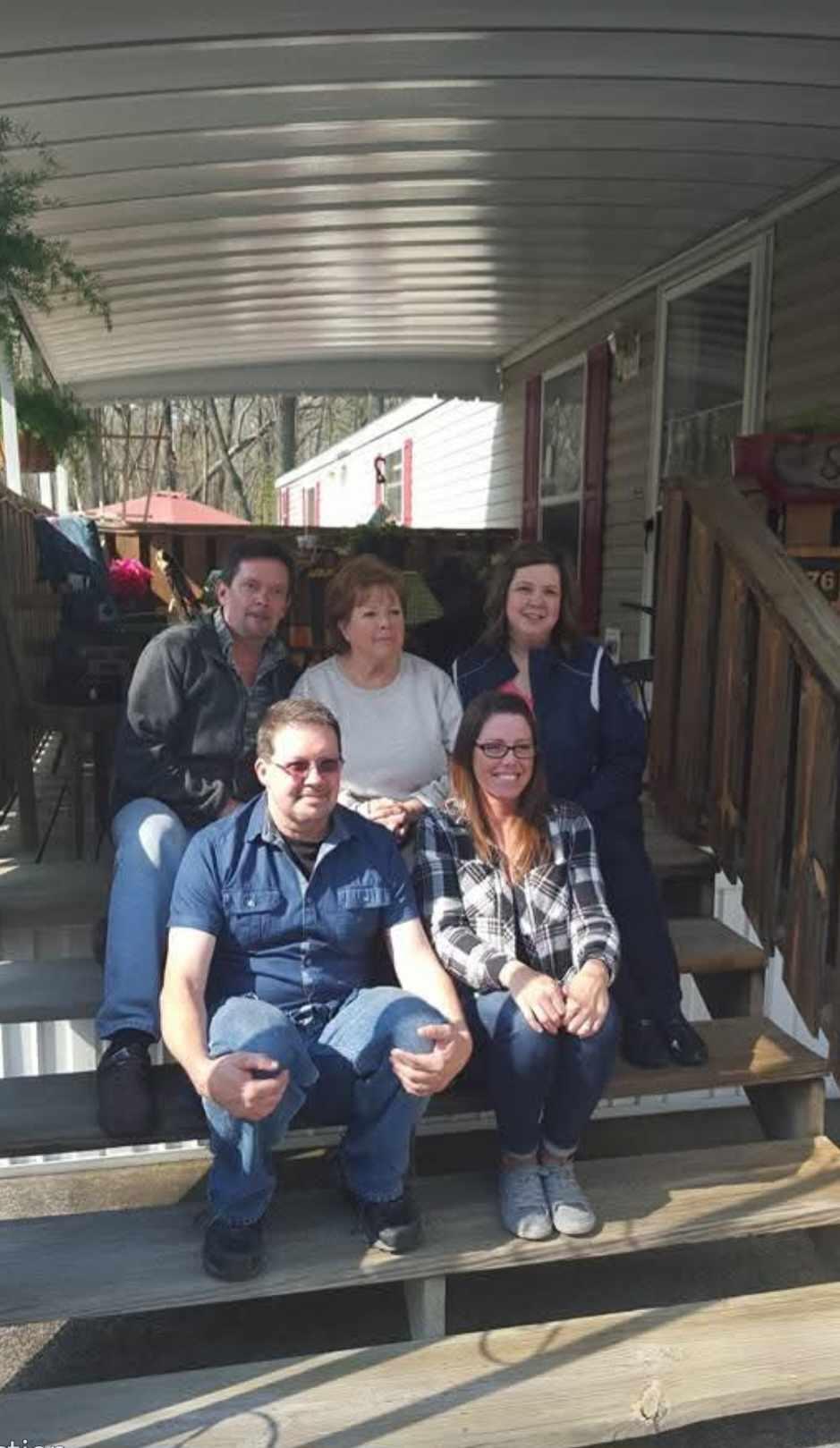 Friends are smiling and sitting together on the steps of a trailer on a sunny day.
