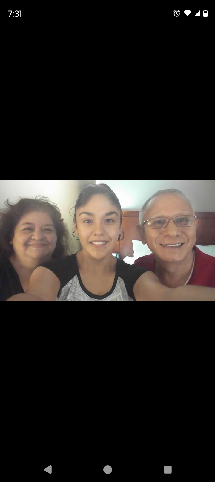 Three family members smile happily together in a warm, informal indoor environment.