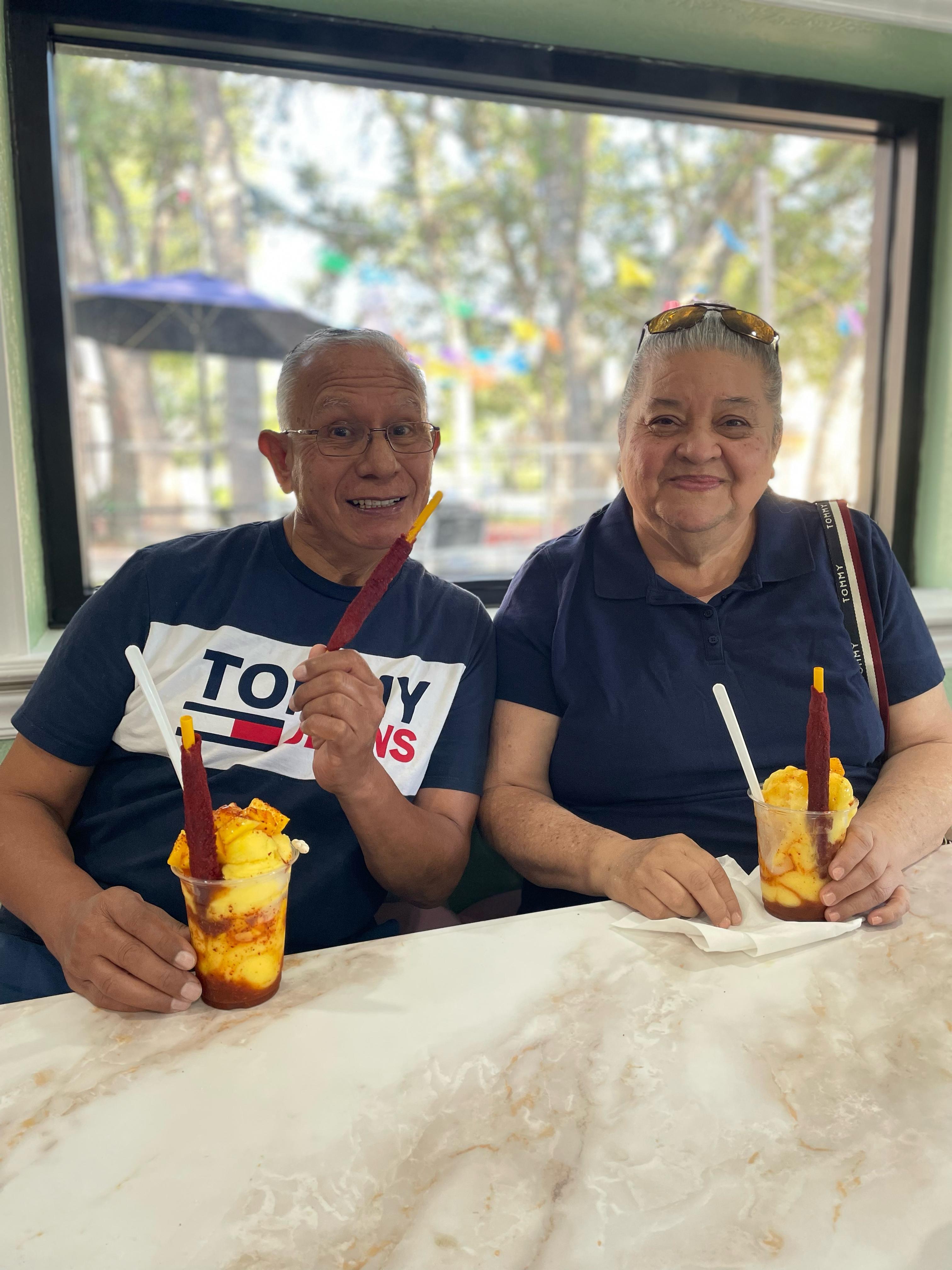Two people sitting together at a table, sipping on colorful tropical drinks and smiling.