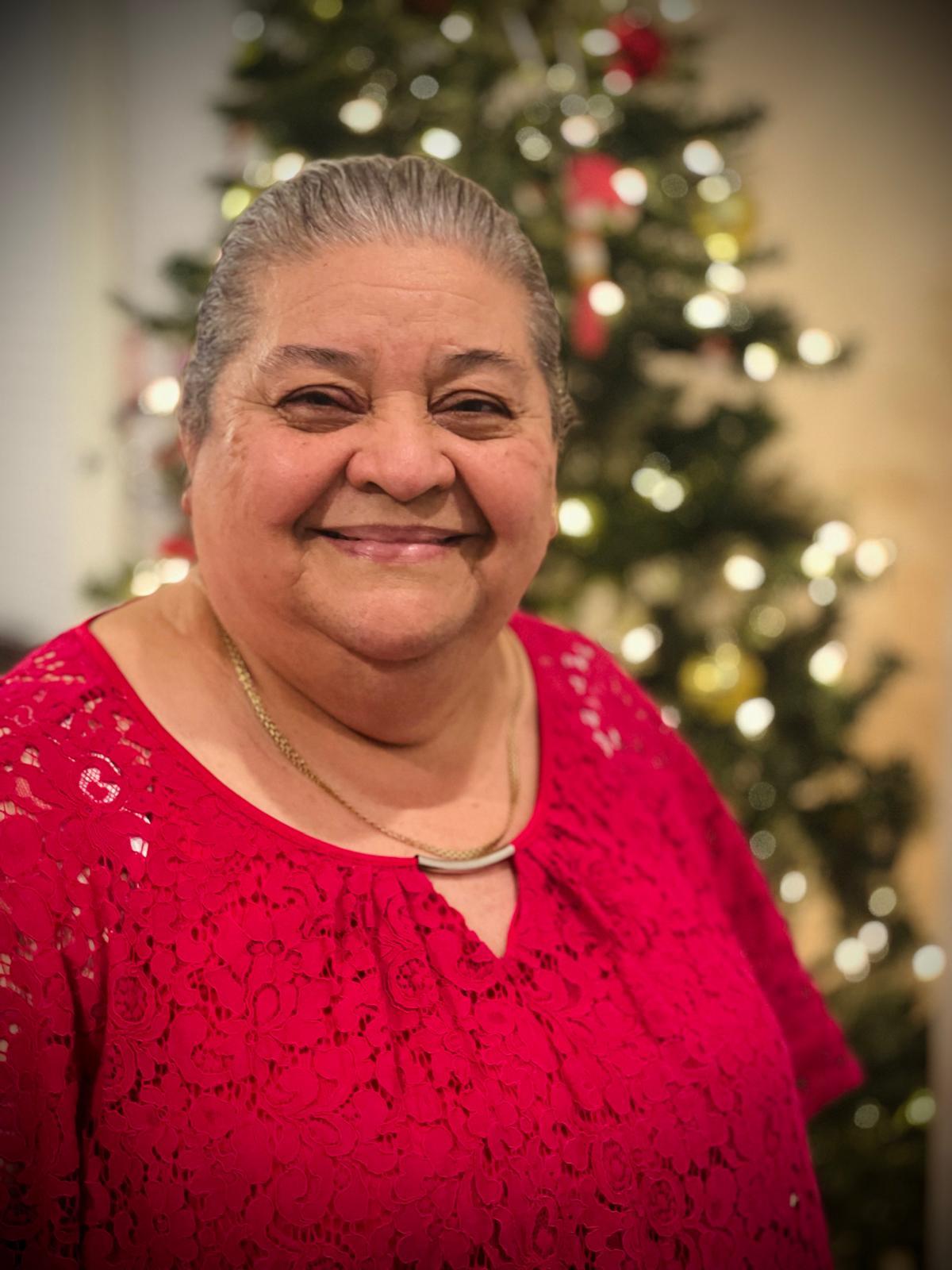 Woman happily poses in a bright red shirt next to a beautifully lit Christmas tree.