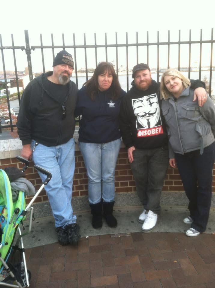 Four friends stand together, smiling and enjoying time outdoors in a casual setting.