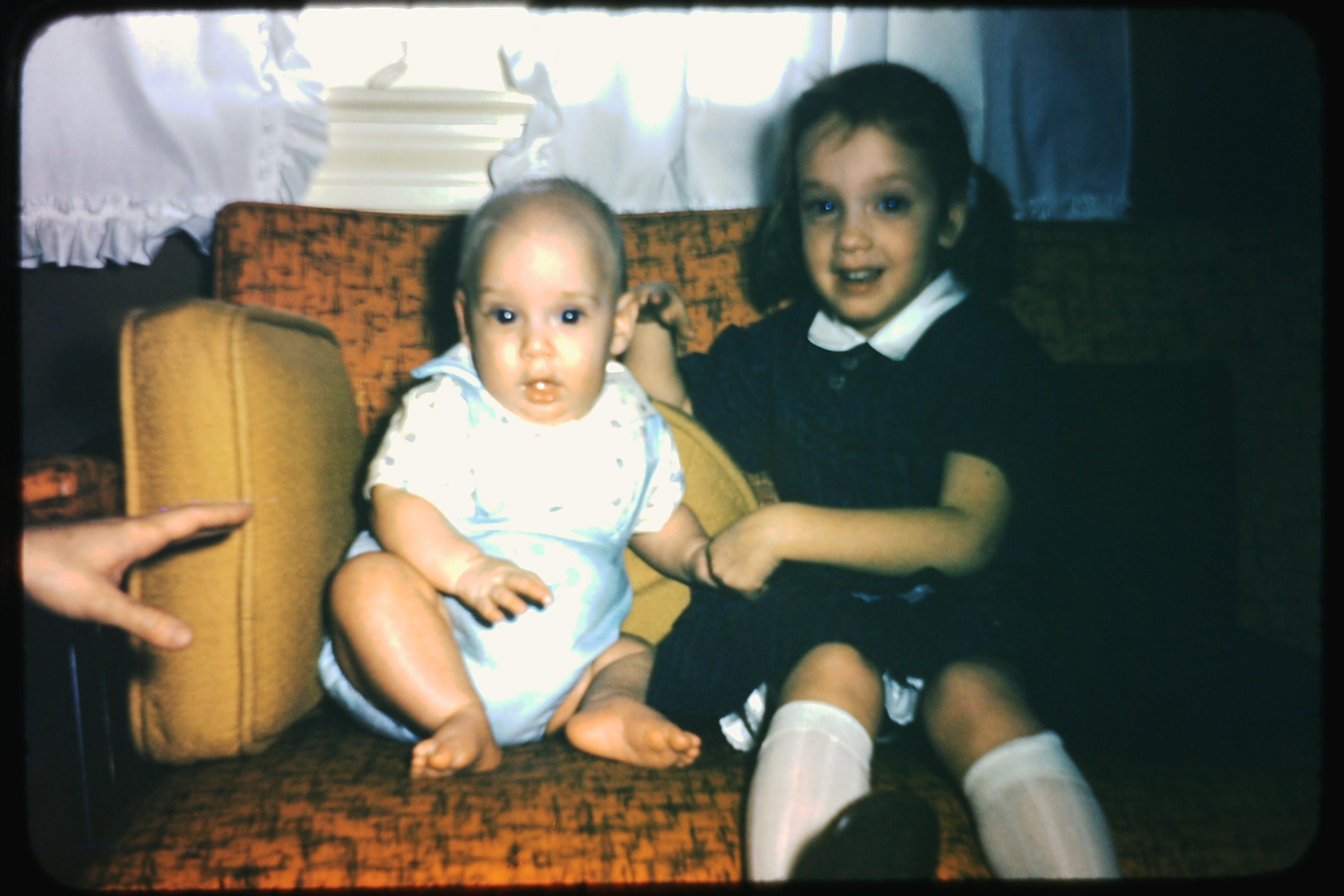 Two young children sit on a soft couch, enjoying playtime in a warm, inviting home setting.
