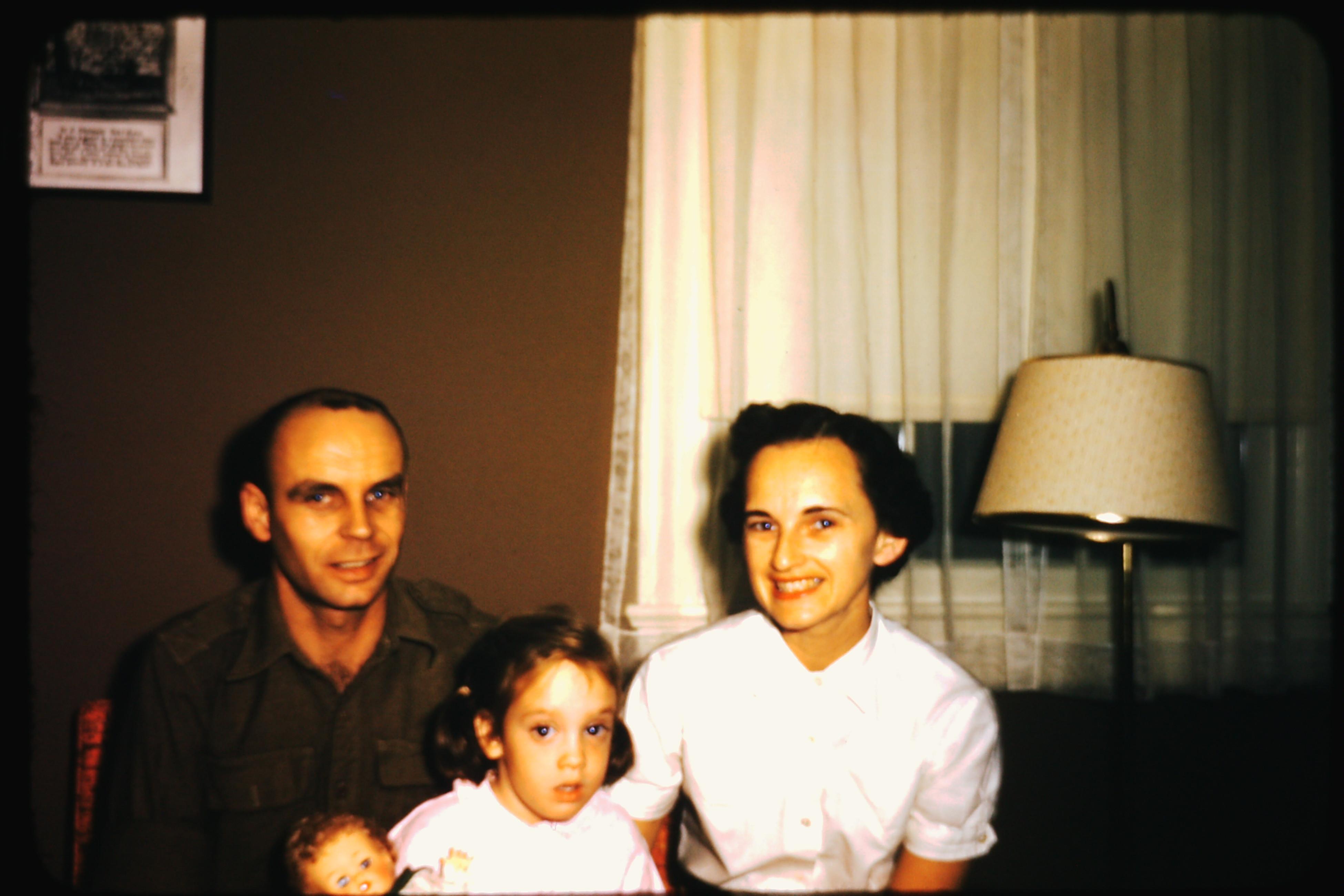 A couple sits on a couch with their child in a warm living room filled with soft lighting.