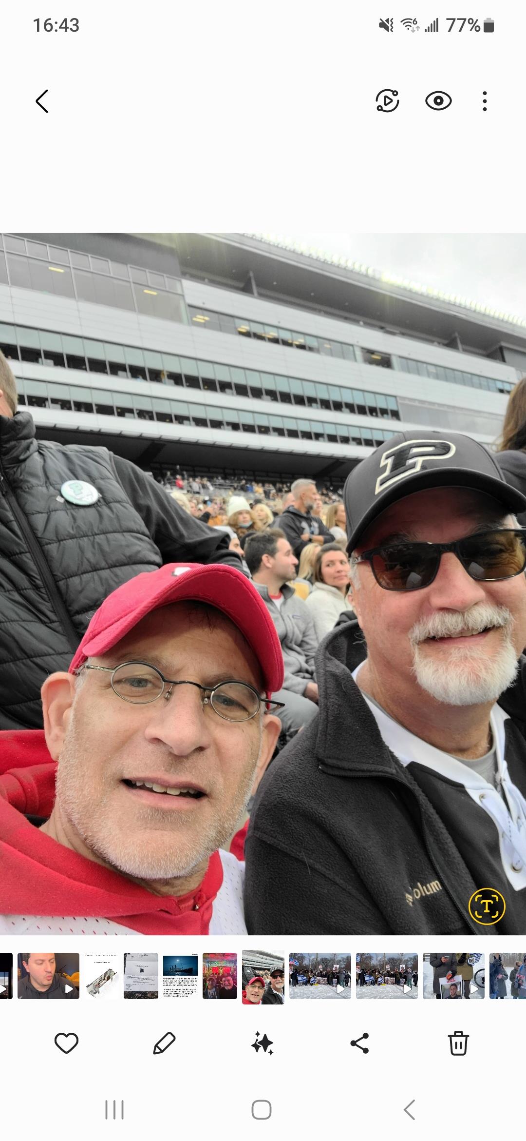 Two friends take a selfie in the stands, surrounded by a lively crowd during a football matchup.
