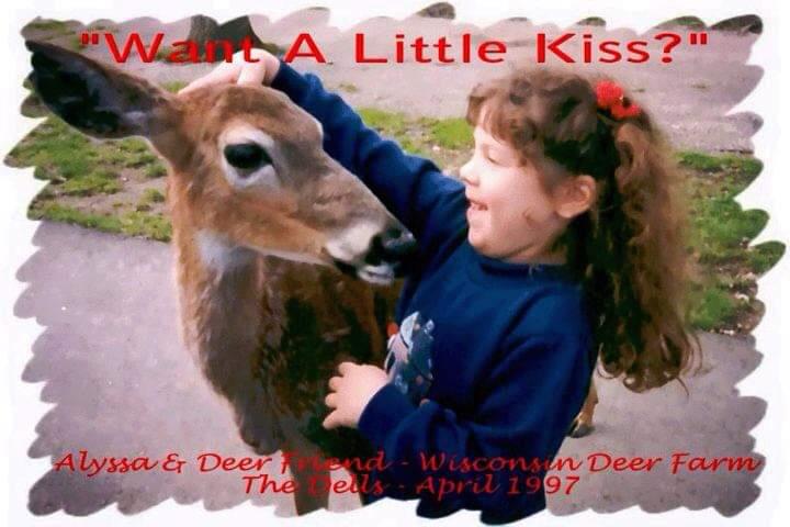 A young girl smiles while affectionately touching a deer in a petting area.