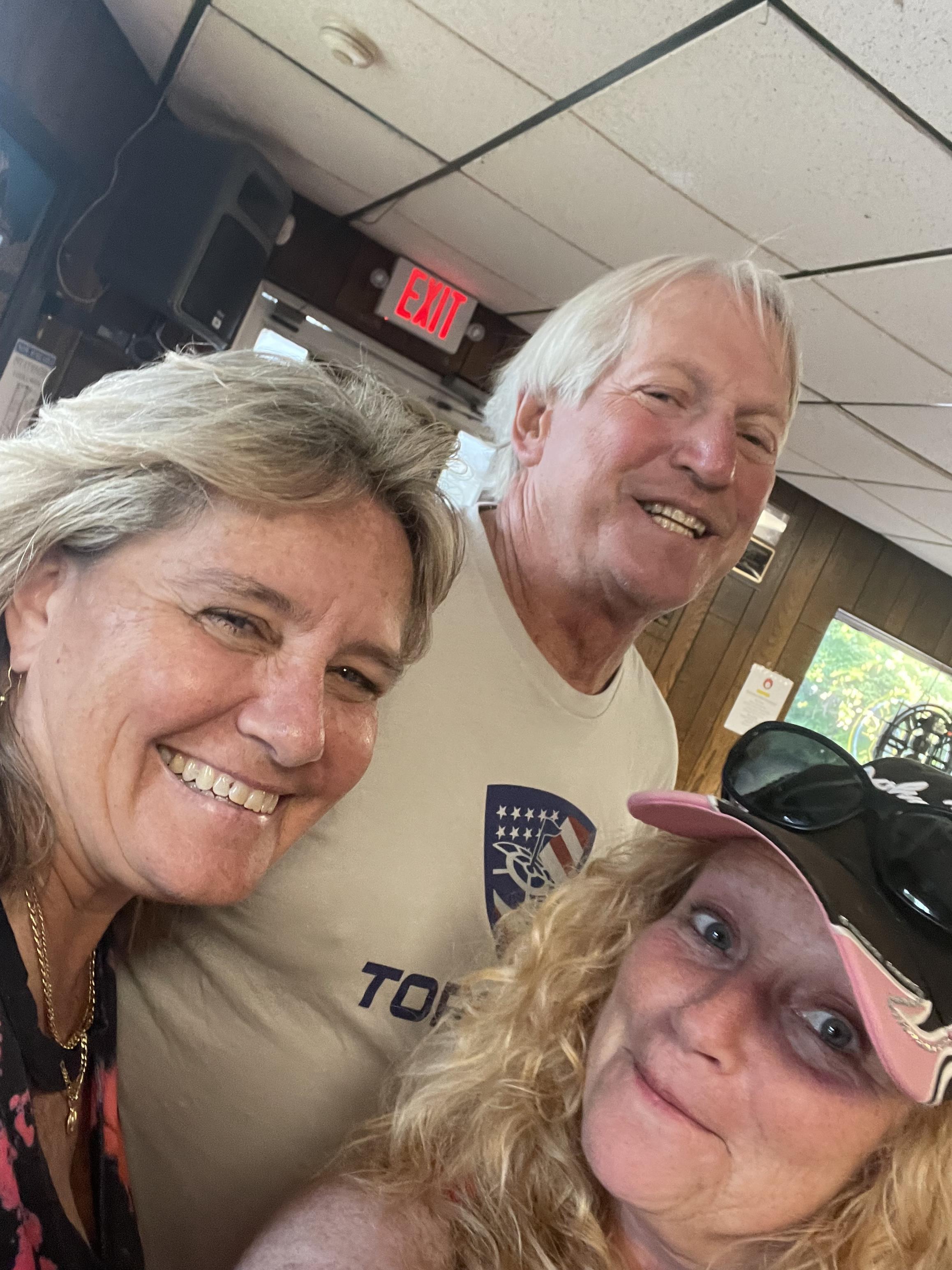 Three friends smiling together at a community center, enjoying their time on a sunny afternoon.