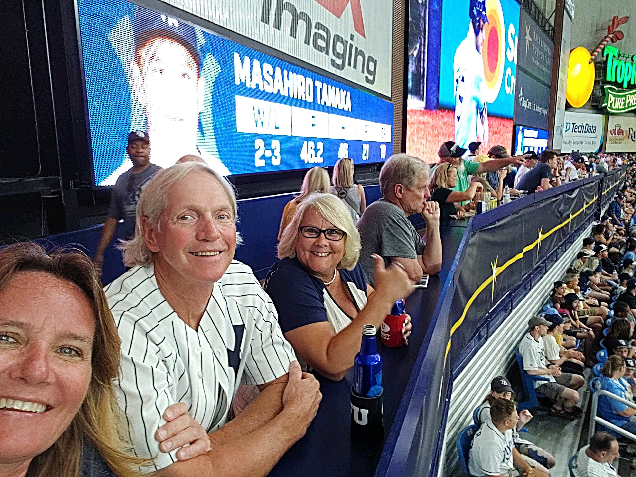 Excited fans gather together, smiling and cheering while watching a baseball game at the stadium.