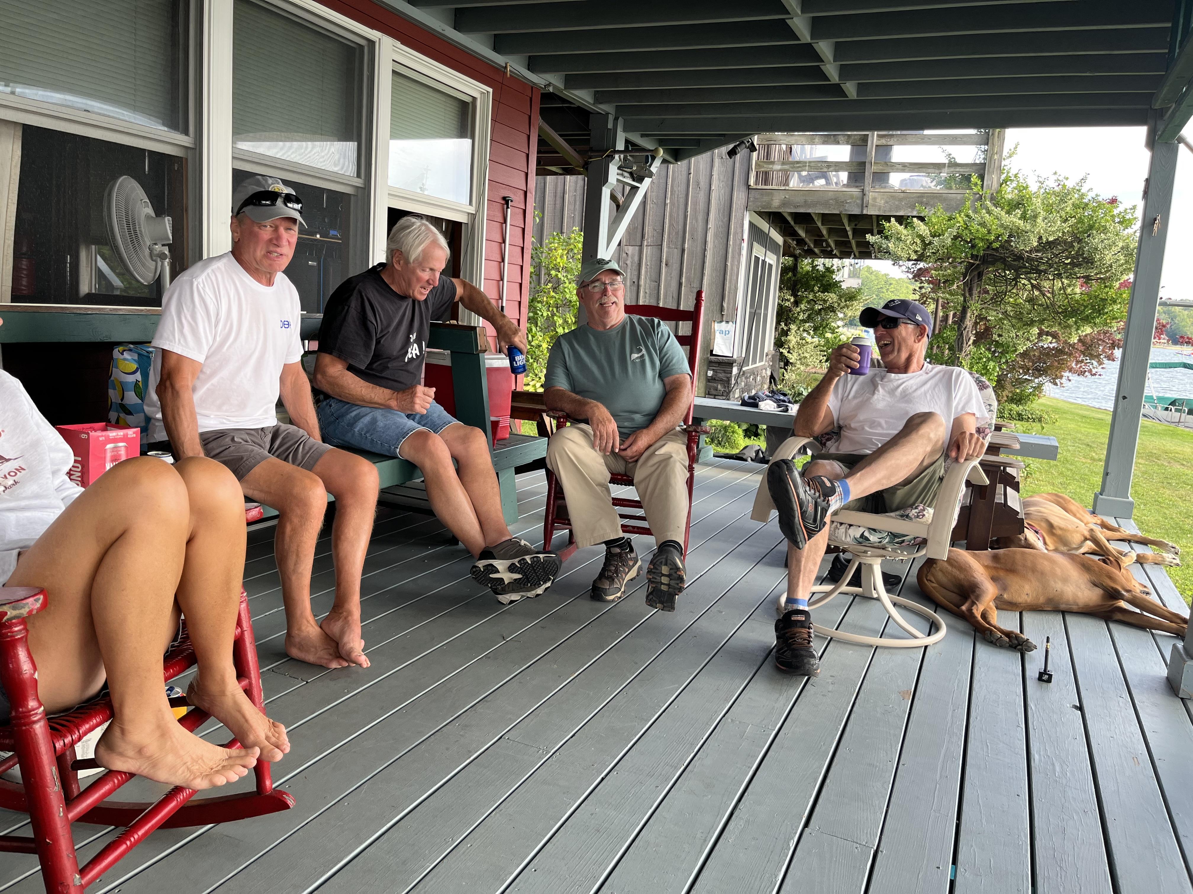 Group of friends chatting and relaxing on a porch while a dog rests nearby on a sunny evening.