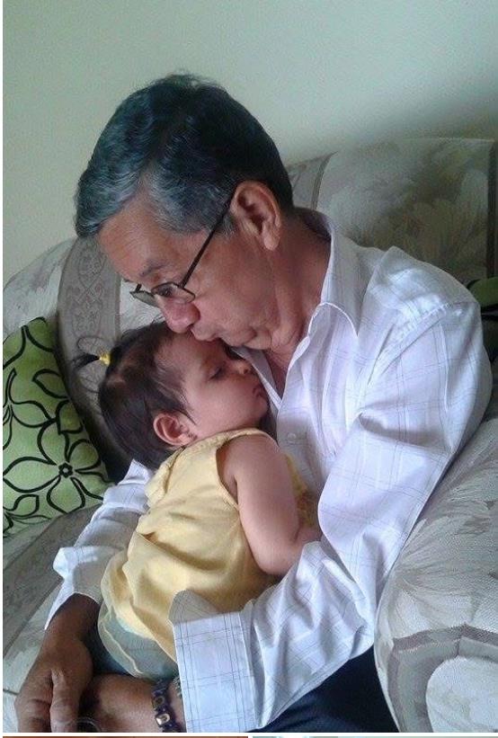 An elderly man lovingly holds his sleeping grandchild on a comfortable couch.