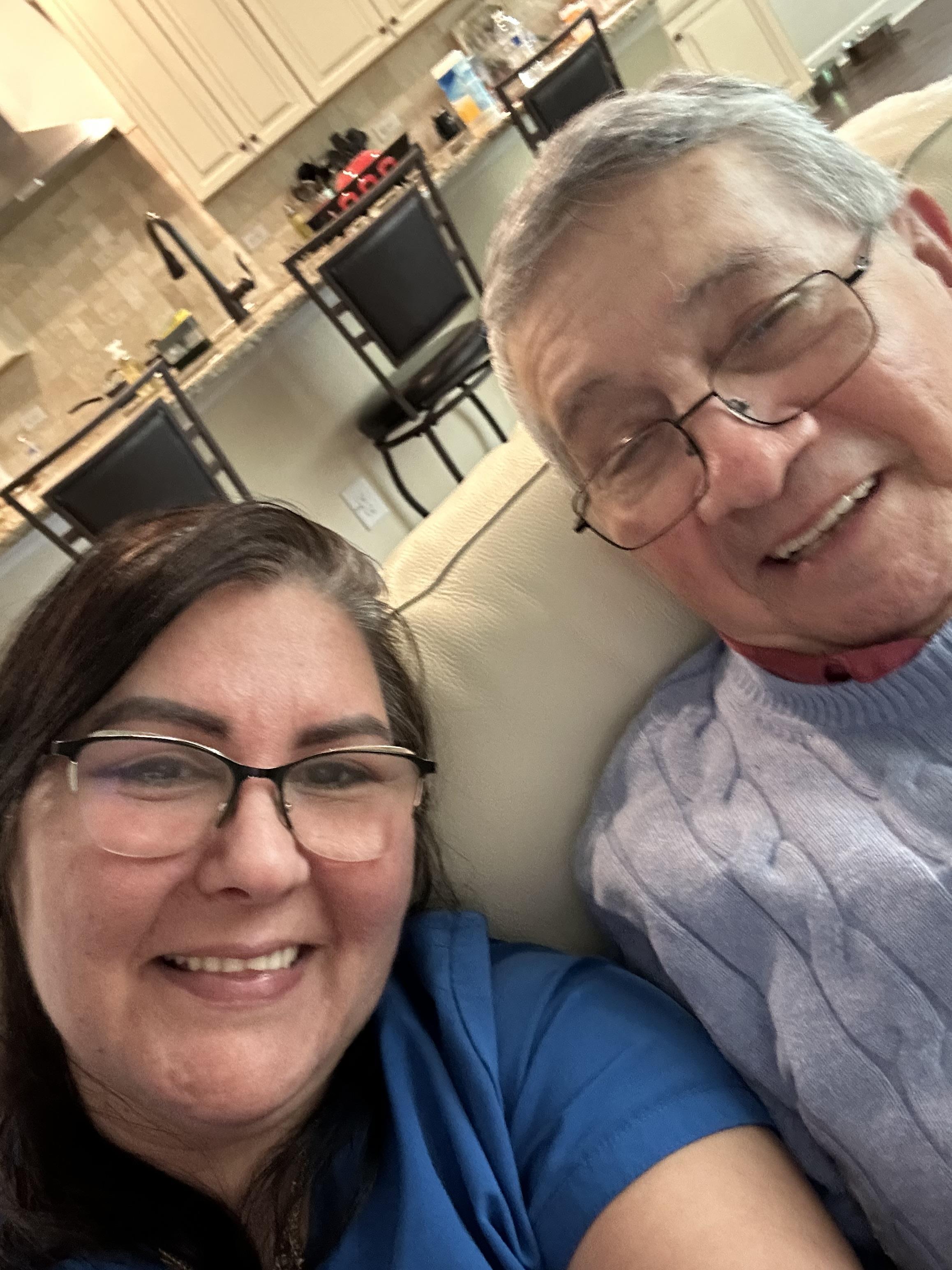 Two family members smile while taking a selfie on a comfortable couch at home.