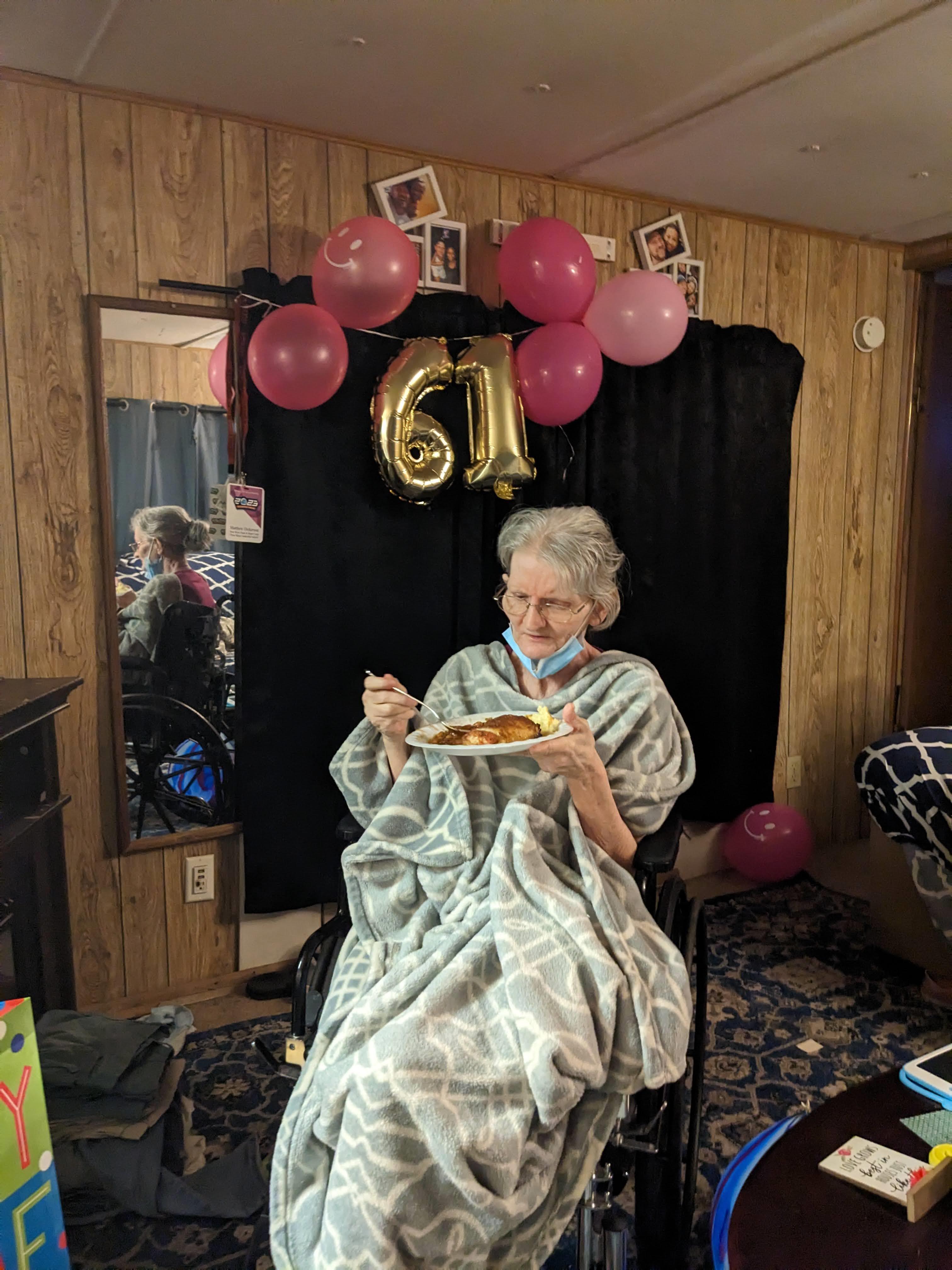 A woman enjoys her birthday cake while wrapped in a soft blanket surrounded by decorations.