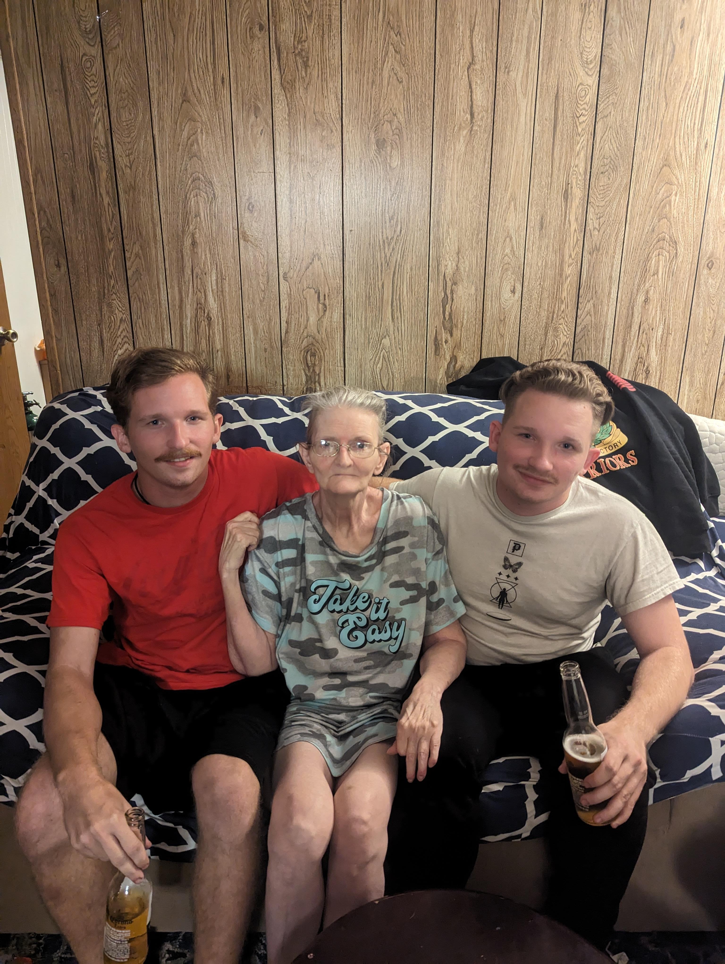 Three family members relax on a couch, sharing drinks and enjoying each other's company.