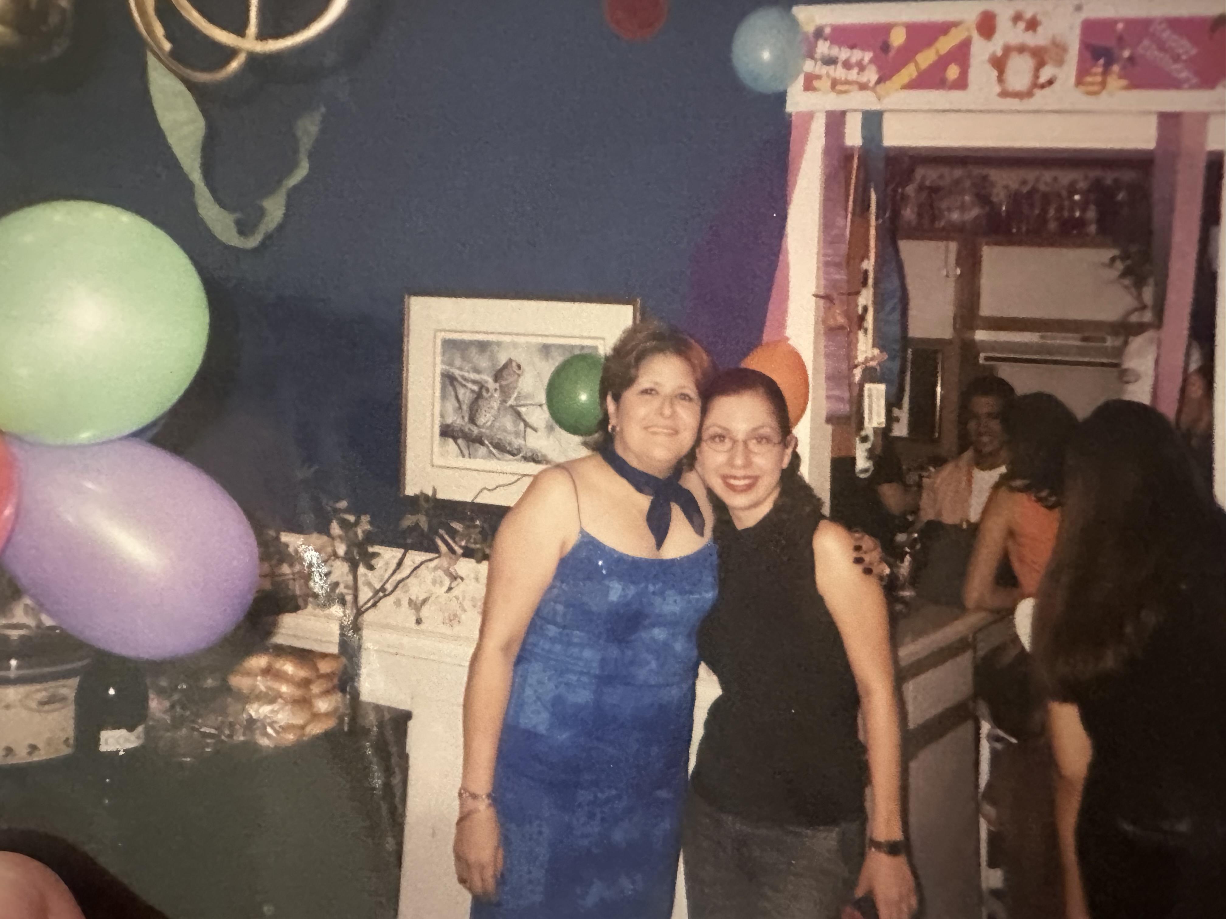 Two friends pose together, celebrating at a festively decorated indoor party.