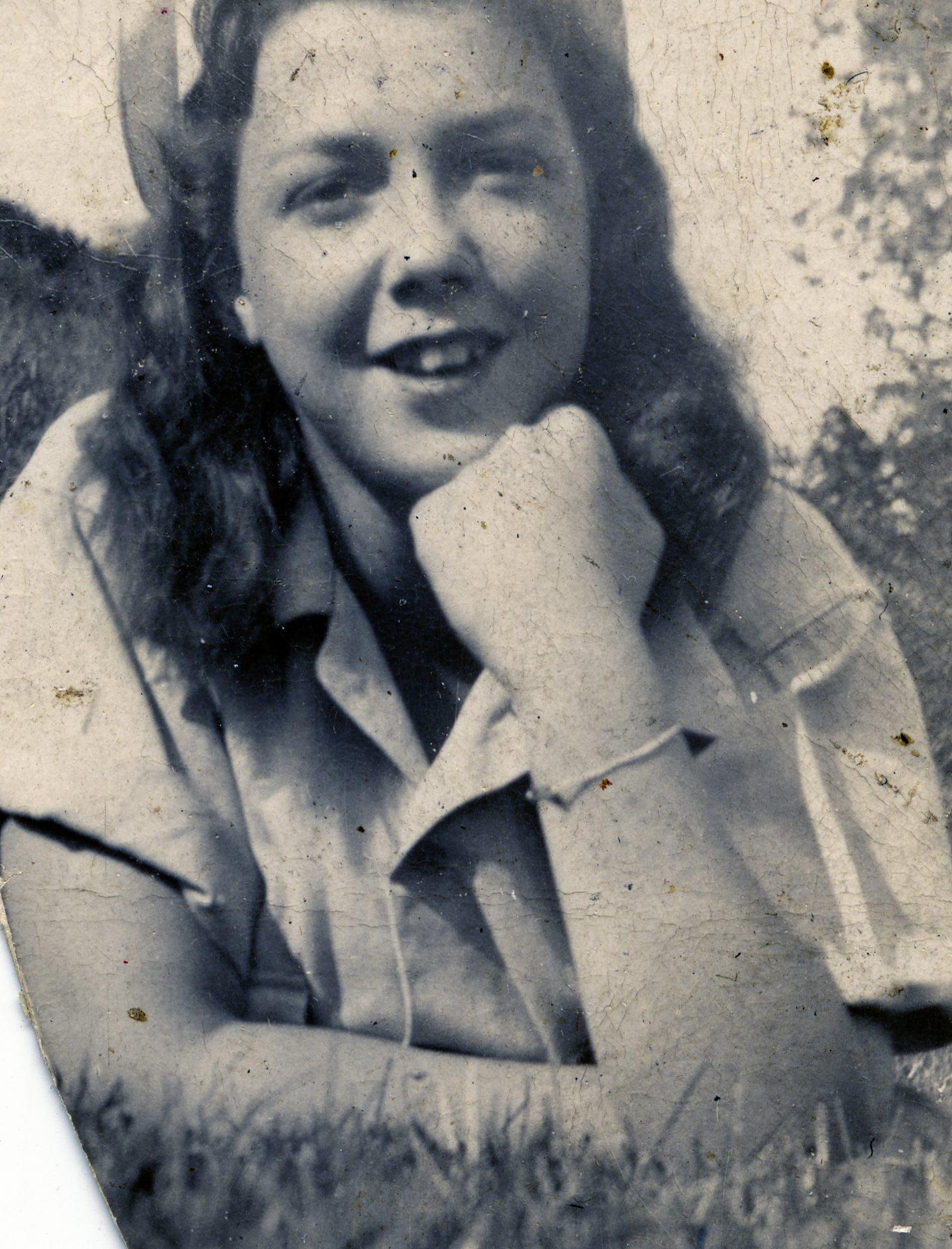 A cheerful young woman relaxes on the grass, smiling with her chin on her hand on a sunny day.